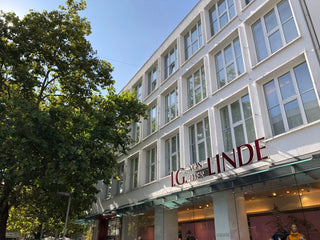 Das Bild zeigt das Geschäftsdgebäude von IG von der Linde in der Hannoverschen Innenstadt. Links ist ein grüner, großer Baum zu sehen, der sich zur der weißen, angestrahlten Fassade des 4 stockigen Hauses neigt.