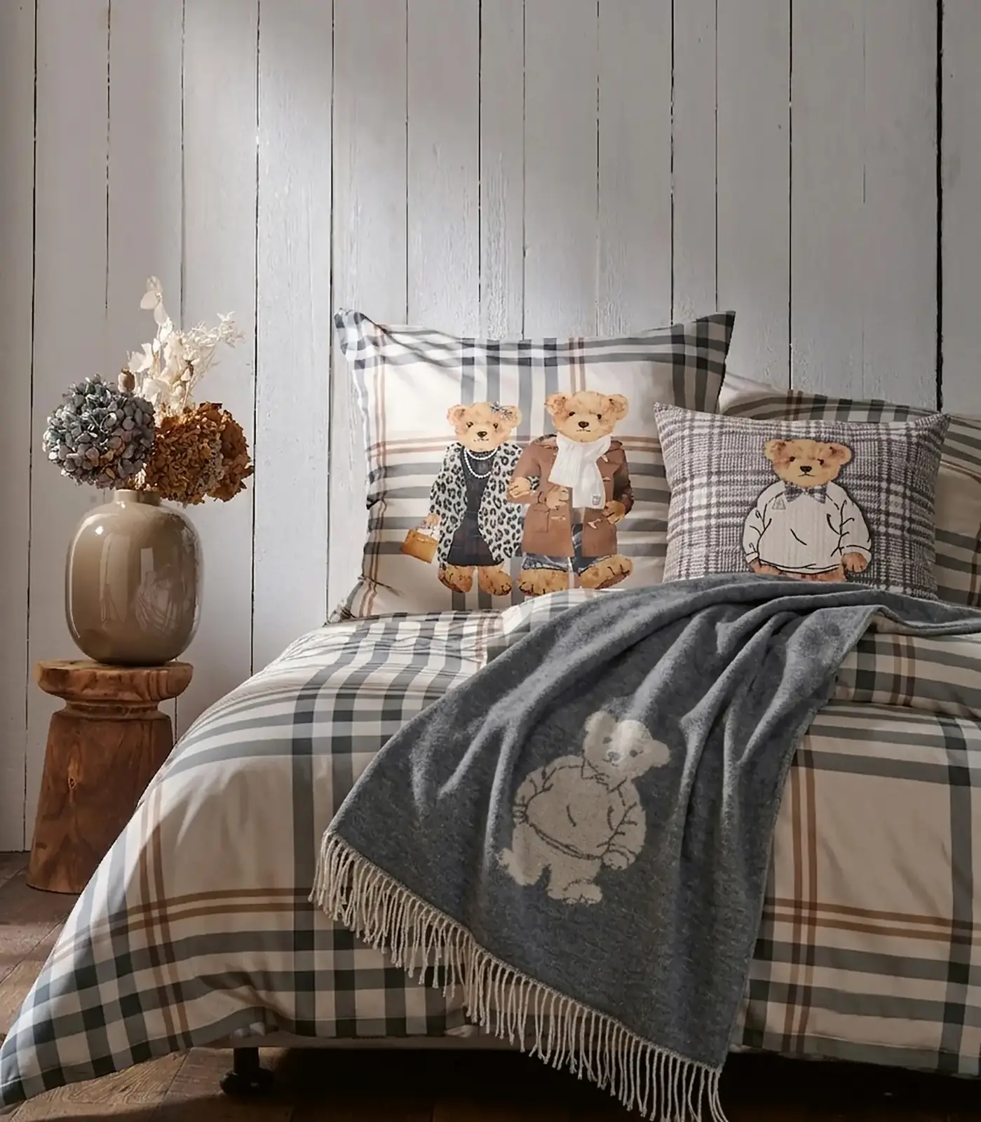 Bett mit Karo-Bettwäsche, Teddy-Kissen und grauem Plaid mit Bärenmotiv